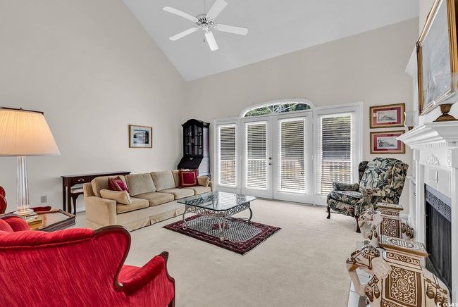 Living room with high vaulted ceiling, a fireplace, ceiling fan, carpet floors, and french doors | Image 4