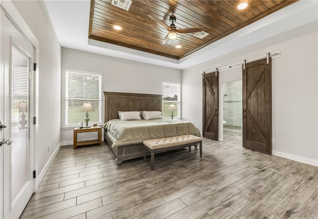 Bedroom with wood ceiling, a raised ceiling, a barn door, wood finished floors, and baseboards | Image 11