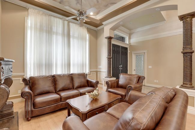 Living area with light wood finished floors, ceiling fan, a raised ceiling, ornamental molding, and arched walkways | Image 6