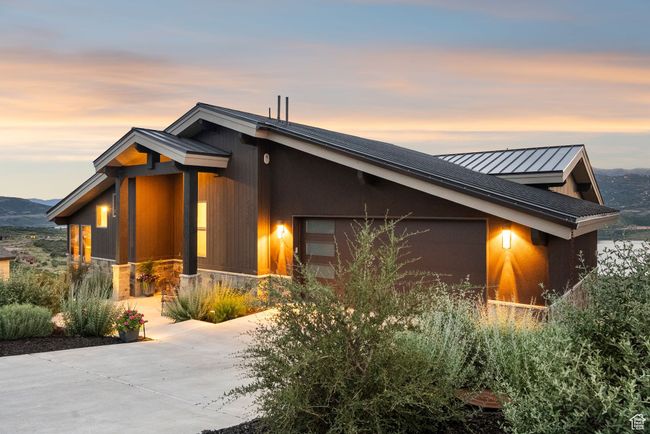 View of side of property featuring driveway, an attached garage, stone siding, a standing seam roof, and a metal roof | Image 67