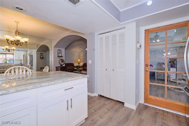 Kitchen with stainless steel refrigerator with ice dispenser, arched walkways, light wood finished floors, light stone counters, and white cabinetry | Image 15