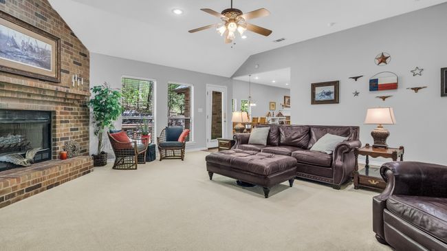 Living area featuring a fireplace, visible vents, ceiling fan, high vaulted ceiling, and light colored carpet | Image 13