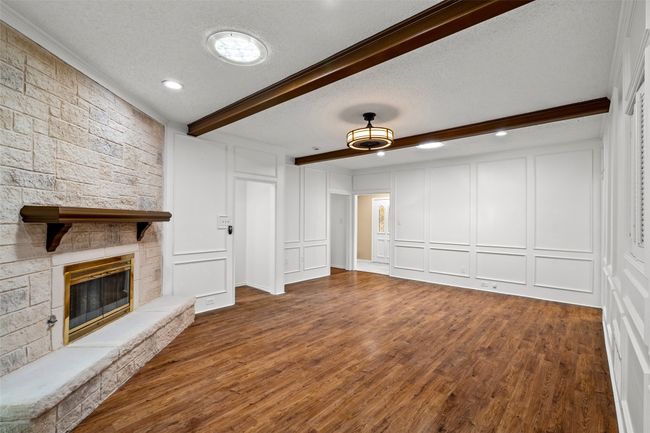 Unfurnished living room featuring a decorative wall, beam ceiling, wood finished floors, a fireplace, and a textured ceiling | Image 8