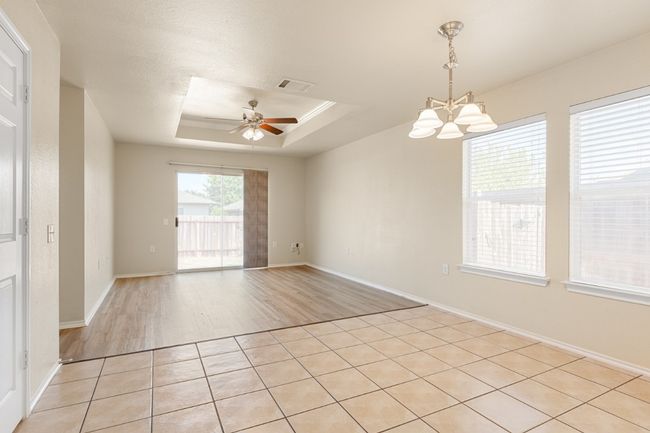 Empty room with a raised ceiling, a chandelier, ceiling fan, and light wood-type flooring | Image 13