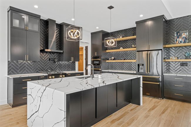 Kitchen with a sink, stainless steel appliances, open shelves, wall chimney range hood, and hanging light fixtures | Image 11