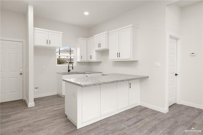 Kitchen with light stone counters, light wood-type flooring, white cabinetry, a peninsula, and recessed lighting | Image 12
