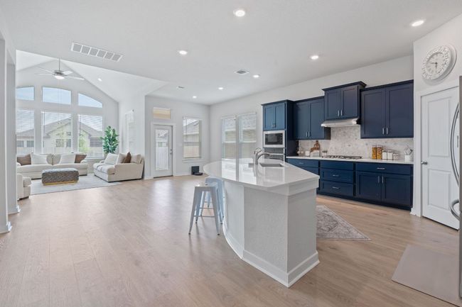 Kitchen with stainless steel appliances, visible vents, blue cabinets, a sink, and decorative backsplash | Image 8