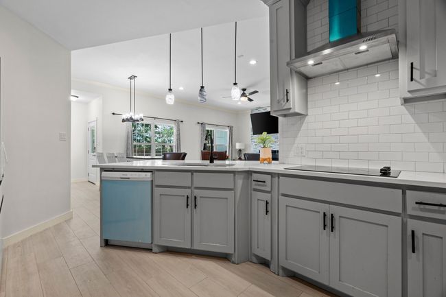 Kitchen with dishwasher, gray cabinets, black electric cooktop, a peninsula, and wall chimney exhaust hood | Image 19
