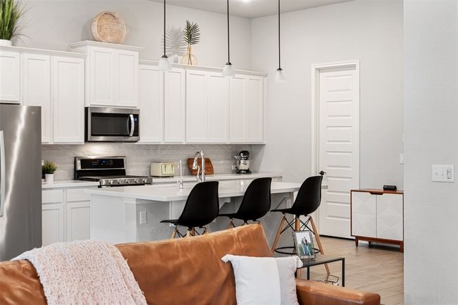 Kitchen featuring stainless steel appliances, backsplash, light wood-style flooring, a kitchen bar, and light countertops | Image 11