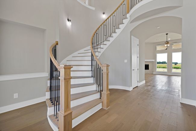 Stairs featuring hardwood / wood-style flooring, a towering ceiling, arched walkways, a stone fireplace, and a ceiling fan | Image 5