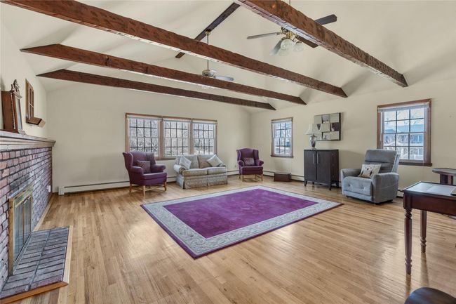 Living area featuring a baseboard radiator, a fireplace, wood finished floors, and lofted ceiling with beams | Image 10