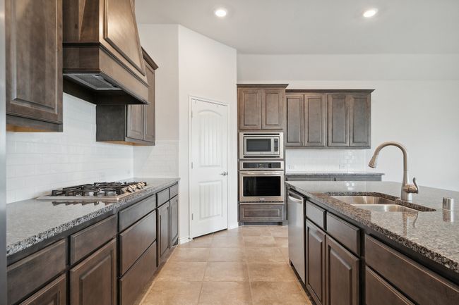 Kitchen with stainless steel appliances, dark stone countertops, premium range hood, dark brown cabinets, and | Image 9