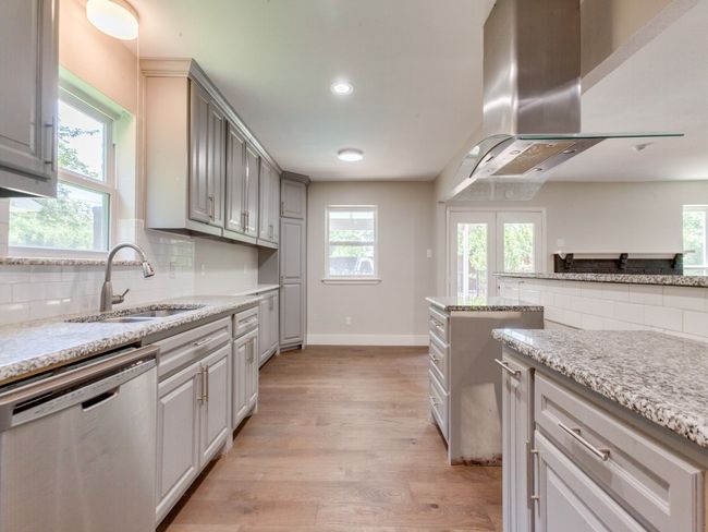 Kitchen with stainless steel dishwasher, a sink, range hood, light wood-style flooring, and decorative backsplash | Image 7