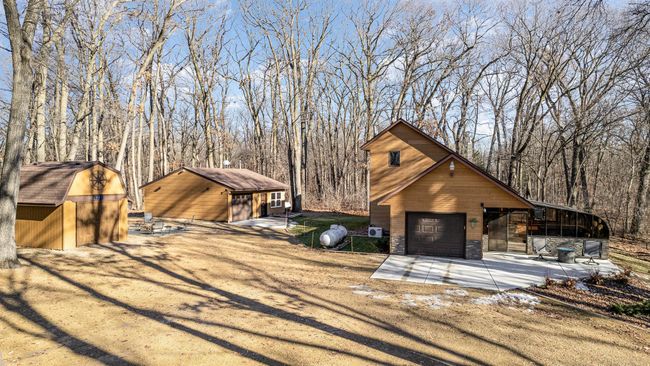 This view is from the 2-car garage looking out at the main house, storage shed, & built-in fire pit. The DREAM workshop garage is insulated & heated & features an 8-ft garage door w/MyQ smart opener. It's bright, light, & clean. | Image 6