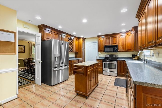 Kitchen with appliances with stainless steel finishes, a kitchen island, light tile patterned flooring, dark countertops, and recessed lighting | Image 10