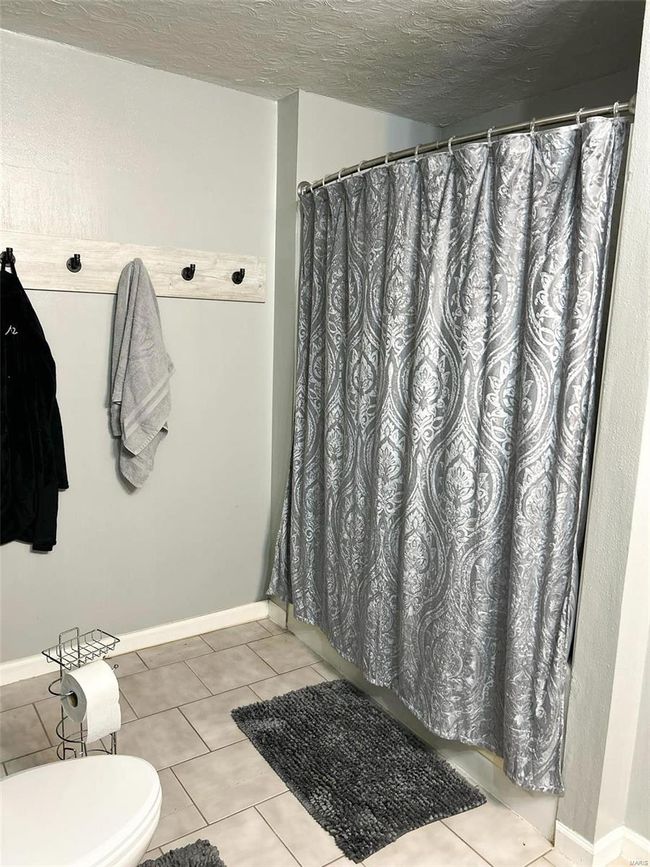 Bathroom with a shower with shower curtain, a textured ceiling, and tile patterned floors | Image 15