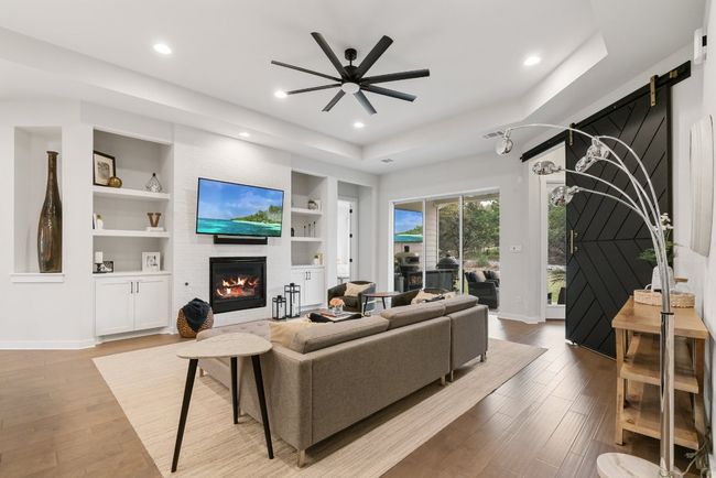 Living room featuring a large fireplace, built in shelves, a ceiling fan, wood finished floors, and recessed lighting | Image 15