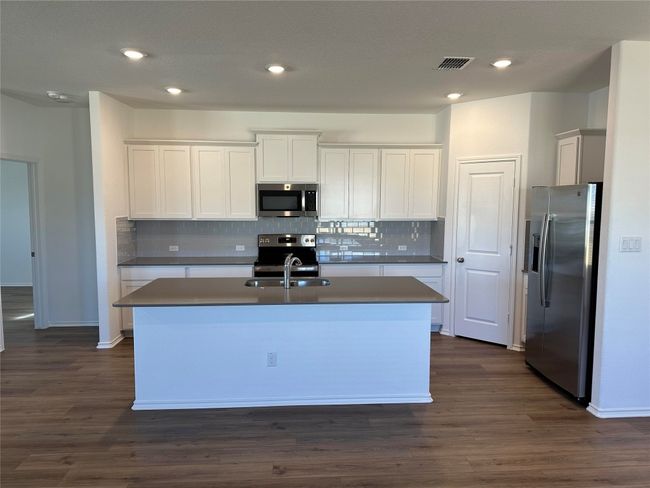 Kitchen with backsplash, visible vents, a sink, stainless steel appliances, and an island with sink | Image 9