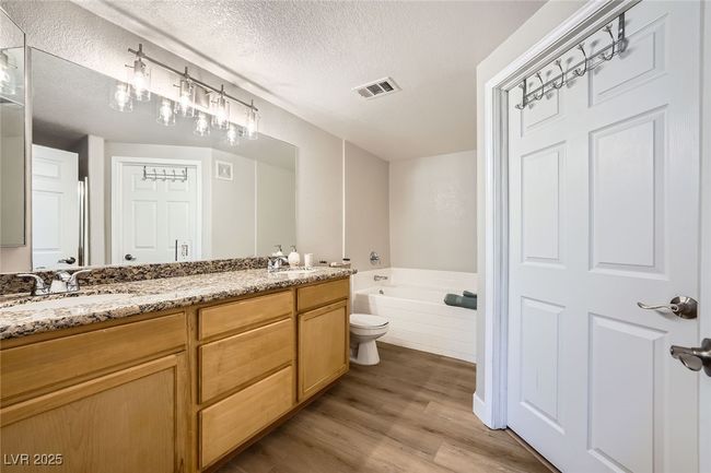 Bathroom with wood finished floors, a sink, a textured ceiling, a bath, and double vanity | Image 16