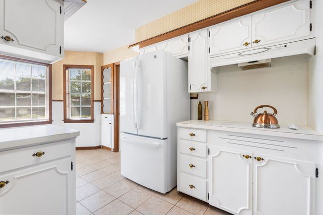 Kitchen featuring freestanding refrigerator, white cabinetry, light tile patterned floors, and under cabinet range hood with a ceramic cooktop. | Image 9
