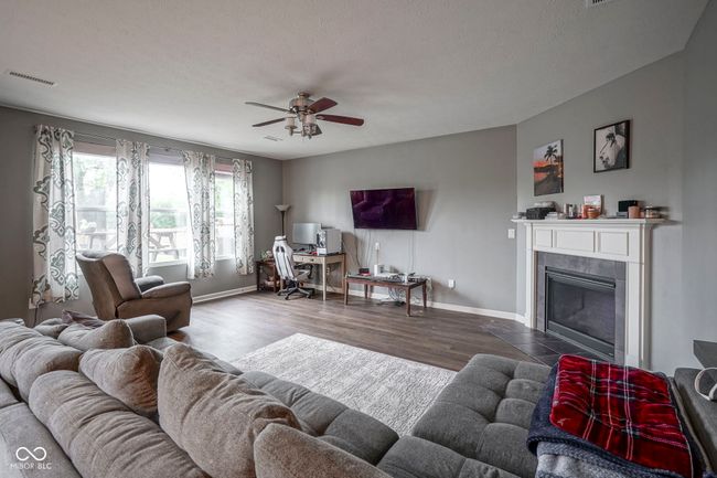 living area featuring baseboards, ceiling fan, wood finished floors, a tile fireplace, and an office area | Image 18