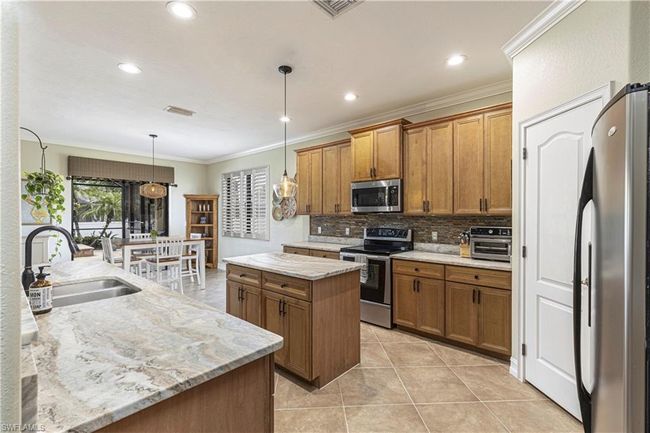 Kitchen with ornamental molding, a sink, a center island, appliances with stainless steel finishes, and brown cabinetry | Image 9