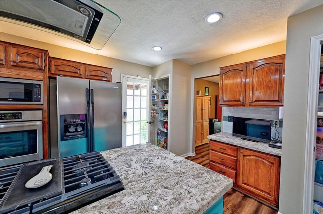 This upgraded kitchen boasts granite countertops, ample cabinet space, two pantries, dual full-size gas ovens, engineered wood floors, and recessed lighting. | Image 17