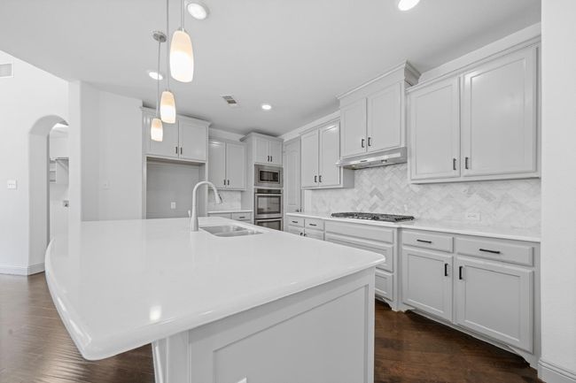 Kitchen with under cabinet range hood, a sink, stainless steel microwave, arched walkways, and gas stovetop | Image 7