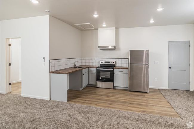 Kitchen featuring light carpet, sink, wall chimney exhaust hood, appliances with stainless steel finishes, and butcher block countertops | Image 36