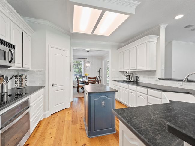 Kitchen with decorative backsplash, dark countertops, crown molding, white cabinets, and appliances with stainless steel finishes | Image 11