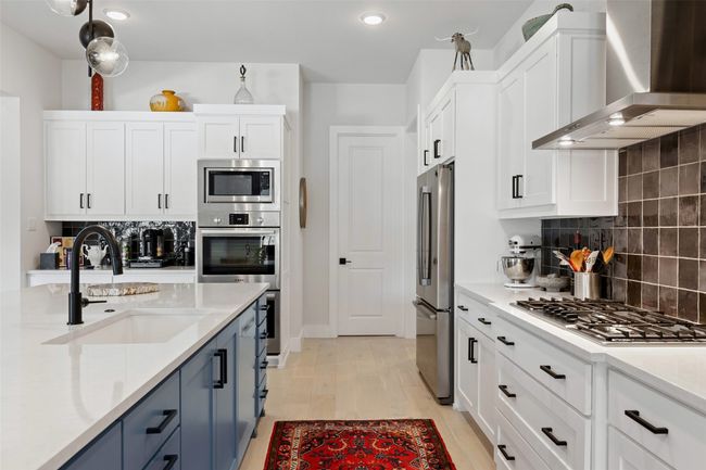 Kitchen with wall chimney range hood, stainless steel appliances, white cabinetry, blue cabinets, and a sink | Image 11