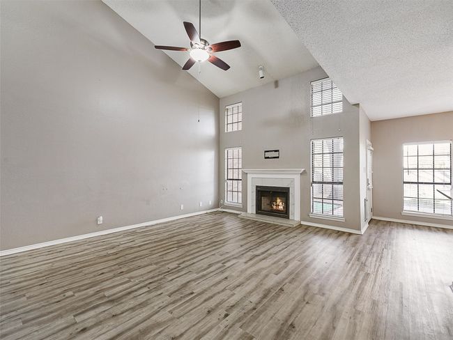 Unfurnished living room featuring a ceiling fan, a textured ceiling, wood finished floors, baseboards, and a tile fireplace | Image 6