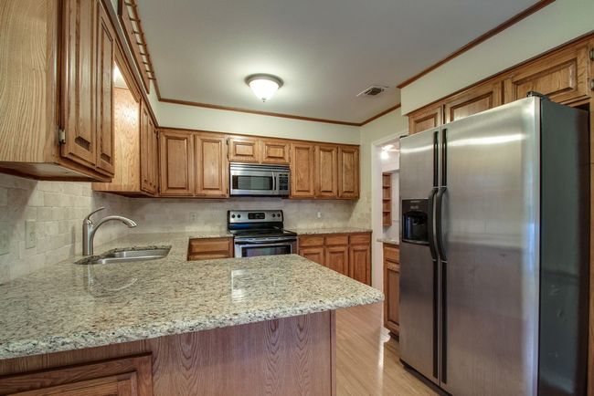 Kitchen featuring stainless steel appliances, light stone countertops, brown cabinetry, light wood-type flooring, and decorative backsplash | Image 12