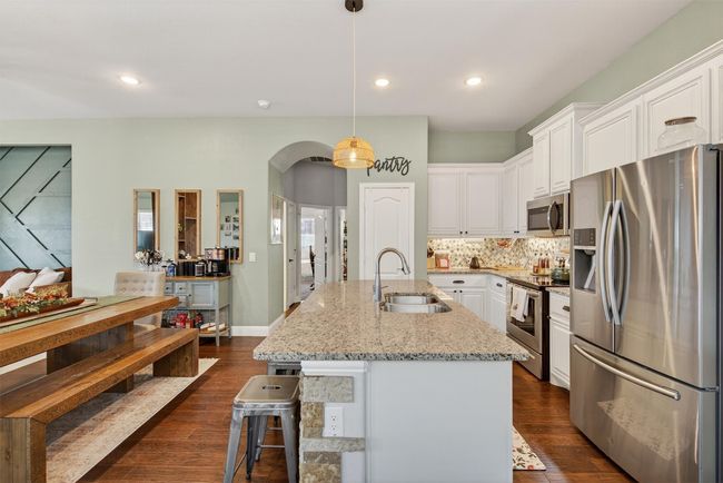 Kitchen featuring appliances with stainless steel finishes, arched walkways, white cabinetry, dark wood-style flooring, and recessed lighting | Image 15