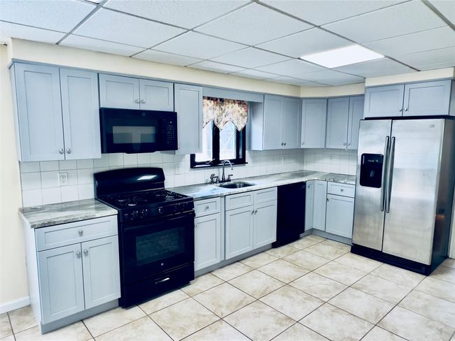 Kitchen with black appliances, backsplash, a drop ceiling, light countertops, and light tile patterned floors | Image 6