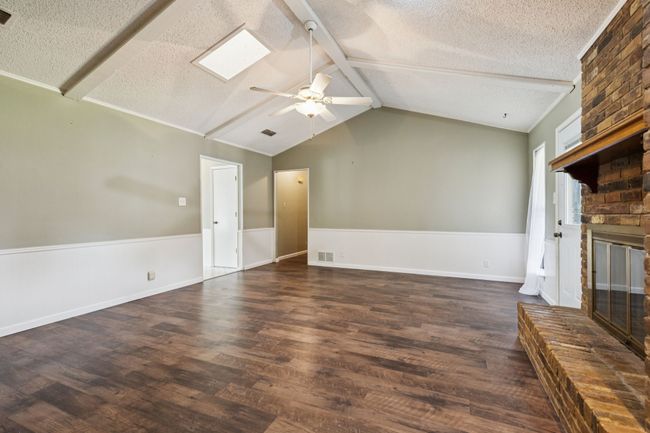 Unfurnished living room with a textured ceiling, a fireplace, wood finished floors, ceiling fan, and a skylight | Image 9
