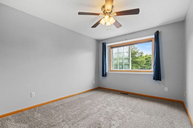 Second bedroom with neutral tones, large window for natural light, and ceiling fan. | Image 18