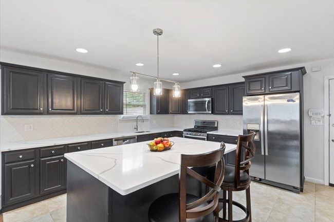 Kitchen with a kitchen island, a sink, pendant lighting, light stone countertops, and appliances with stainless steel finishes | Image 37