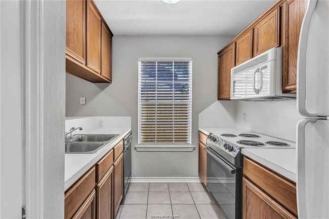 Kitchen featuring white appliances, light countertops, light tile patterned floors, and brown cabinets | Image 8