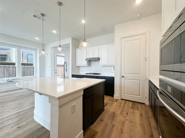 Kitchen featuring appliances with stainless steel finishes, light wood-style floors, light countertops, white cabinetry, and backsplash | Image 13