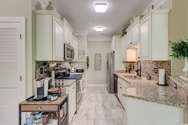 Kitchen with decorative backsplash, light stone counters, stainless steel appliances, and a sink | Image 5