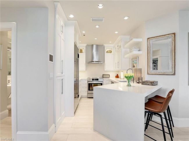 Kitchen with wall chimney exhaust hood, stove, a sink, a peninsula, and white cabinets | Image 14