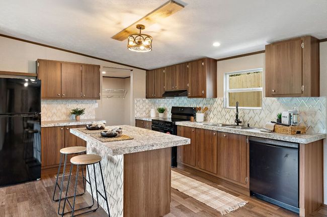 Kitchen featuring under cabinet range hood, light countertops, a sink, black appliances, and tasteful backsplash | Image 15