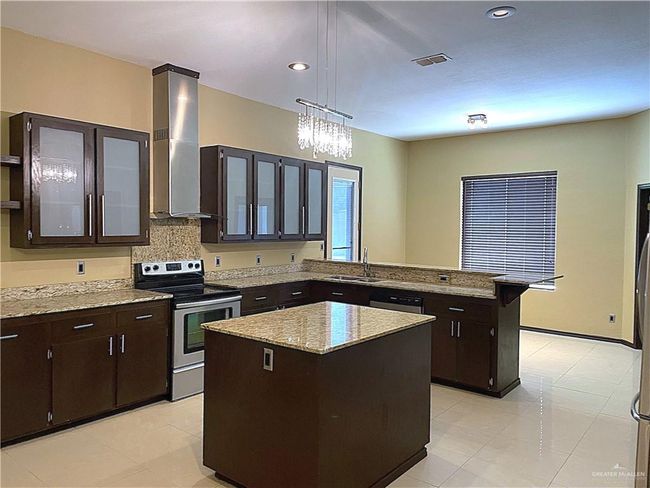 Kitchen featuring stainless steel appliances, wall chimney range hood, a sink, a peninsula, and a center island | Image 7