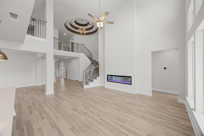 Unfurnished living room featuring a towering ceiling, light wood-style floors, stairway, ceiling fan, and baseboards | Image 7