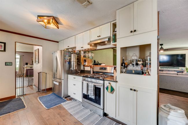 Kitchen with dark countertops, white cabinetry, under cabinet range hood, light wood-style flooring, and stainless steel appliances | Image 11