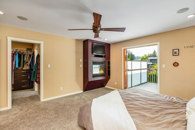 Carpeted bedroom featuring a glass covered fireplace, a walk in closet, recessed lighting, ceiling fan, and French doors to outside | Image 16