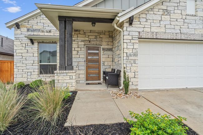 View of exterior entry with stone siding, board and batten siding, a garage, and fence | Image 4
