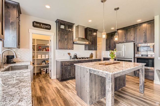 Kitchen featuring wall chimney exhaust hood, stainless steel appliances, dark brown cabinets, light wood-style floors, and recessed lighting | Image 7