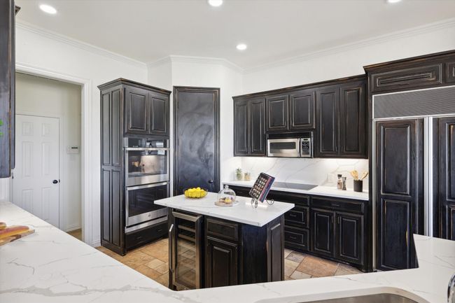 Kitchen featuring beverage cooler, appliances with stainless steel finishes, light stone countertops, stone tile floors, and ornamental molding | Image 15